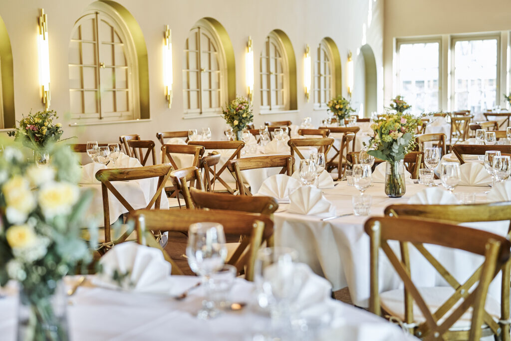 Eleganter Speisesaal mit Holzst&uuml;hlen, gedeckten Tischen und Blumenarrangements in Vasen. Lichtdurchfluteter Raum.