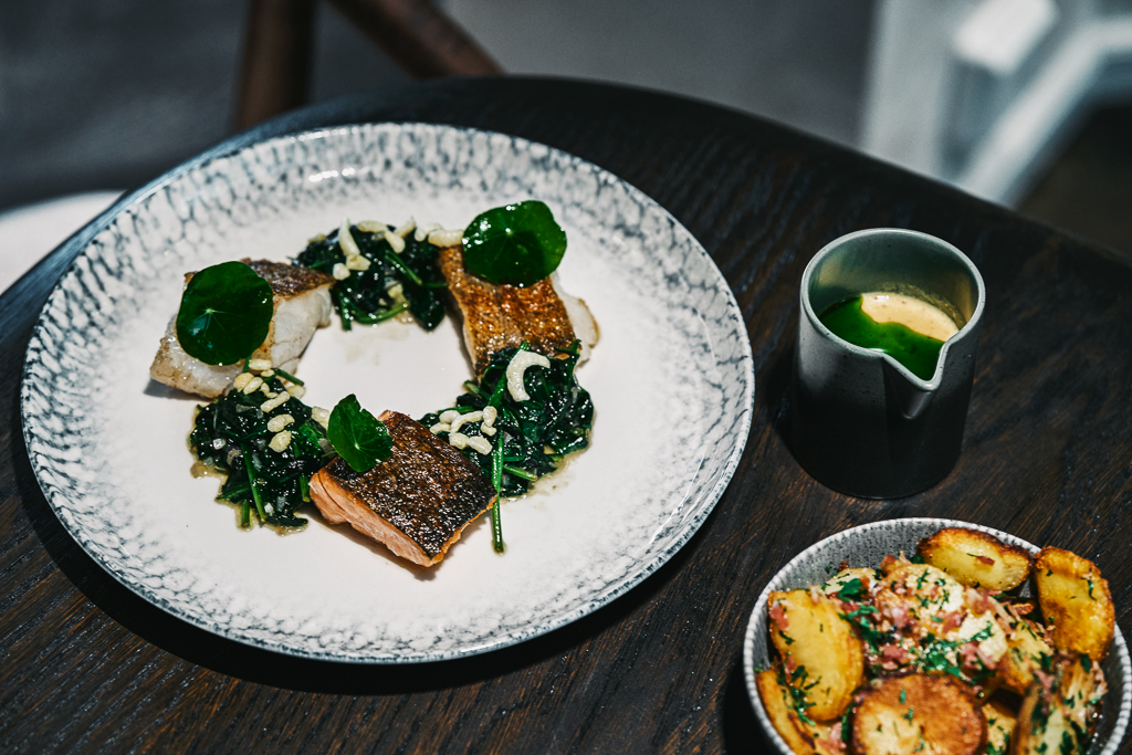 Ein Teller mit gebratenem Fischfilet, Spinat und gr&uuml;ner Sauce, daneben eine Schale mit Kartoffeln.