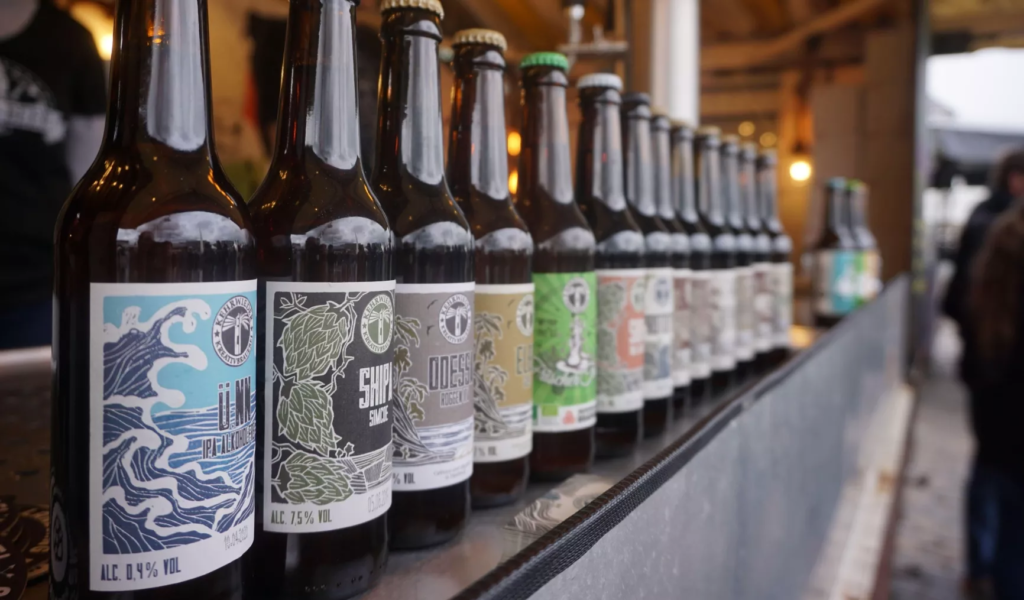 Reihe von Bierflaschen mit verschiedenen Etiketten und Alkoholgehalt, auf einem Tisch in einer Brauerei.