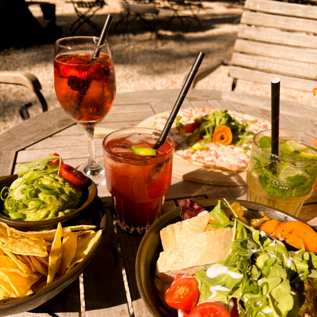 Ein Tisch im Freien mit verschiedenen Gerichten: Guacamole, Nachos, Salat und zwei Cocktails.