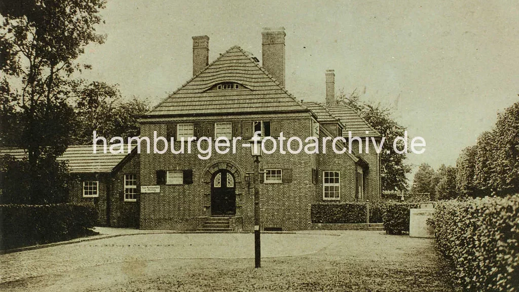 Historisches Backsteinhaus mit Satteldach, umgeben von B&auml;umen und gepflegten Hecken.