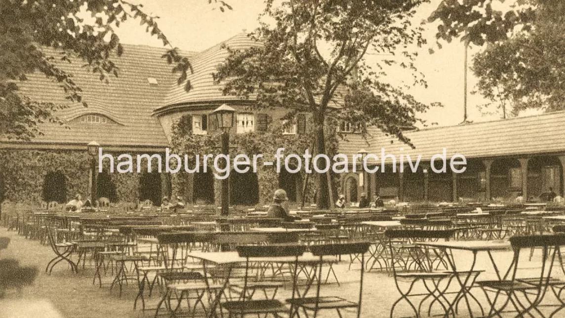 Eine historische Au&szlig;enansicht eines Caf&eacute;s mit leeren Tischen und St&uuml;hlen unter B&auml;umen.