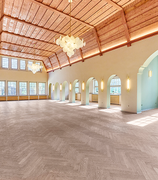 Ger&auml;umiger Saal mit Holzbalkendecke, gro&szlig;en Fenstern und eleganten Kronleuchtern. Helle, freundliche Atmosph&auml;re.