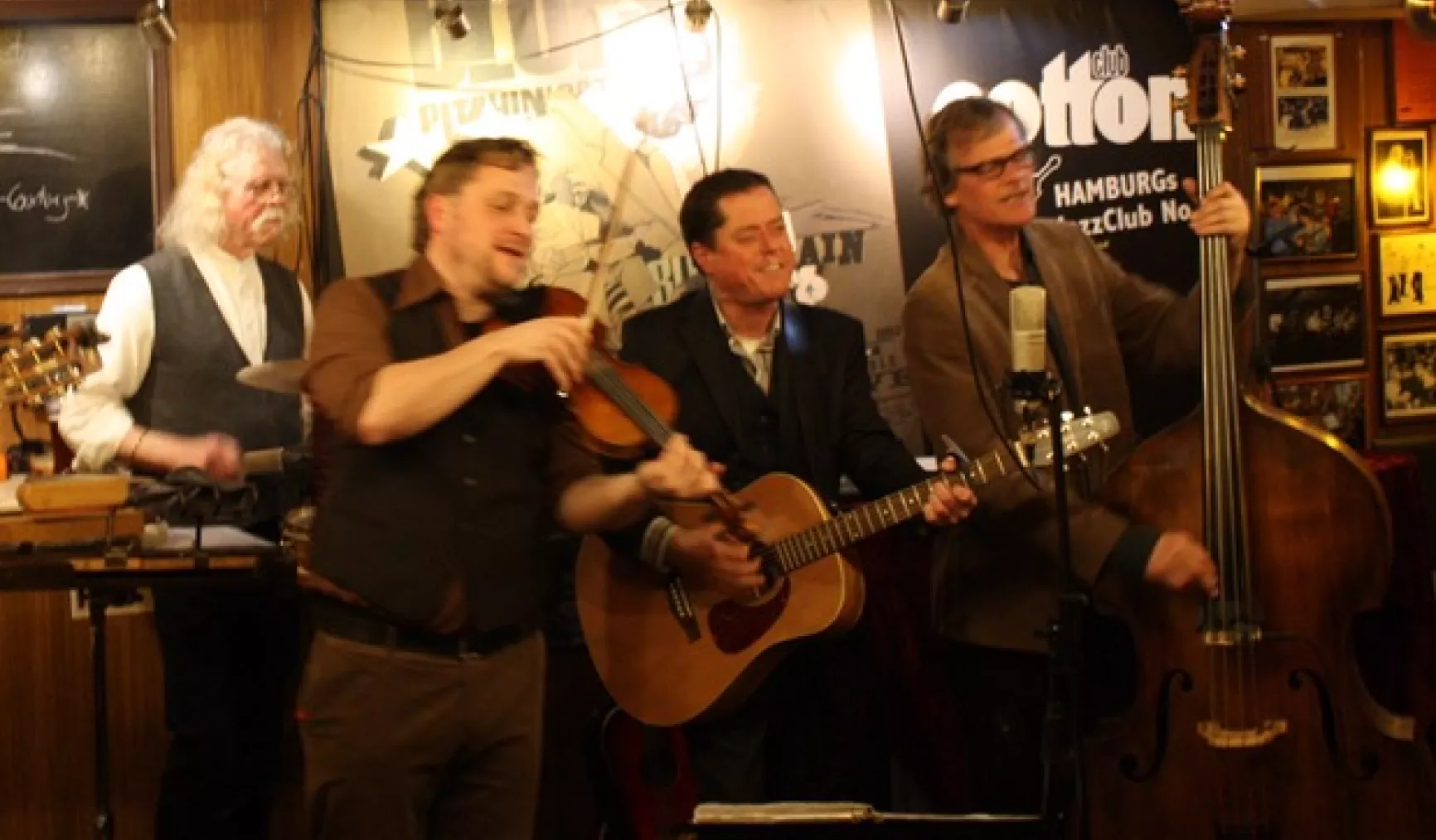 Eine Band spielt live in einem Jazzclub, mit Geige, Gitarre und Kontrabass, umgeben von einer gemütlichen Atmosphäre.