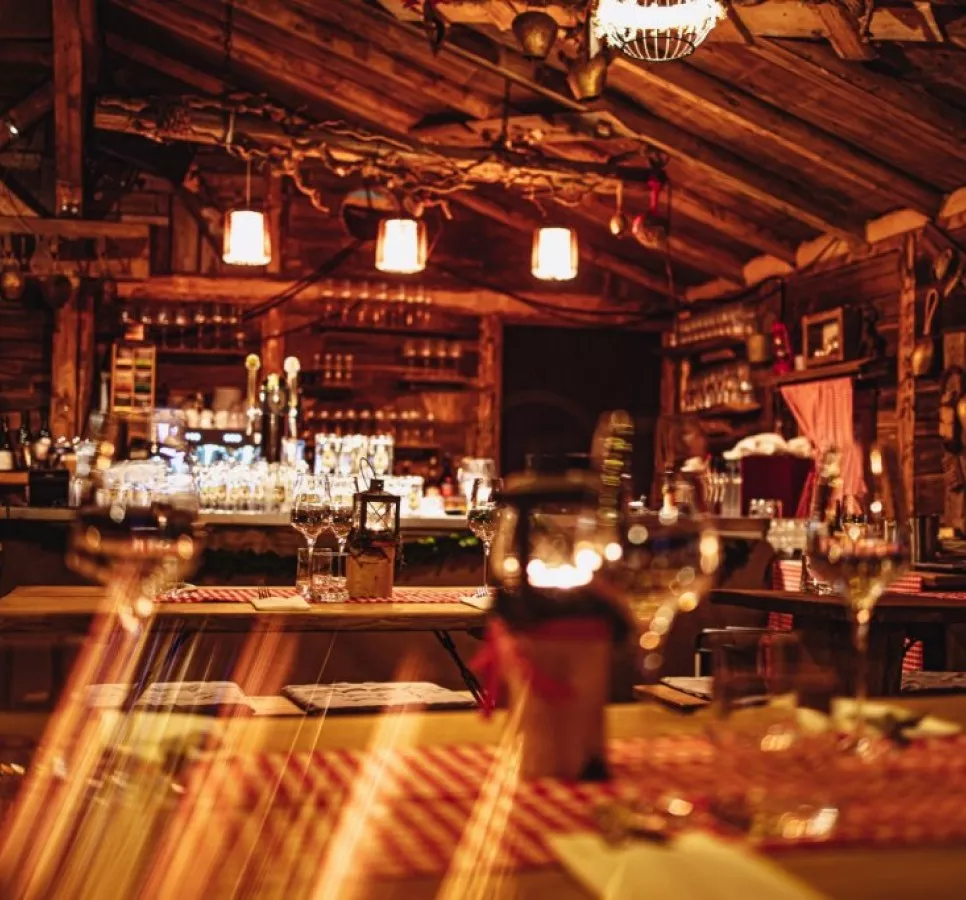 Gem&uuml;tliches Restaurant mit Holzdekor, beleuchtet von h&auml;ngenden Lampen und Gl&auml;sern auf den Tischen.