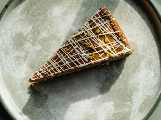 Ein St&uuml;ck Kuchen auf einem grauen Teller, dekoriert mit wei&szlig;er Schokolade und Pistazienst&uuml;ckchen.