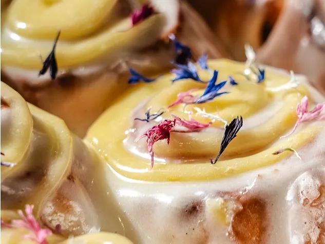 Zimtrollen mit cremigem Zuckerguss und essbaren Bl&uuml;ten dekoriert.