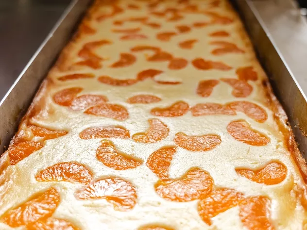 Ein Blechkuchen mit einer cremigen Schicht und dekorativen Mandarinenst&uuml;cken auf der Oberfl&auml;che.
