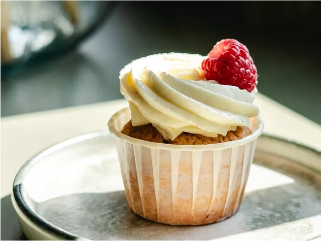 Ein Cupcake mit Vanillecreme und einer Himbeere auf der Spitze, serviert auf einem silbernen Teller.