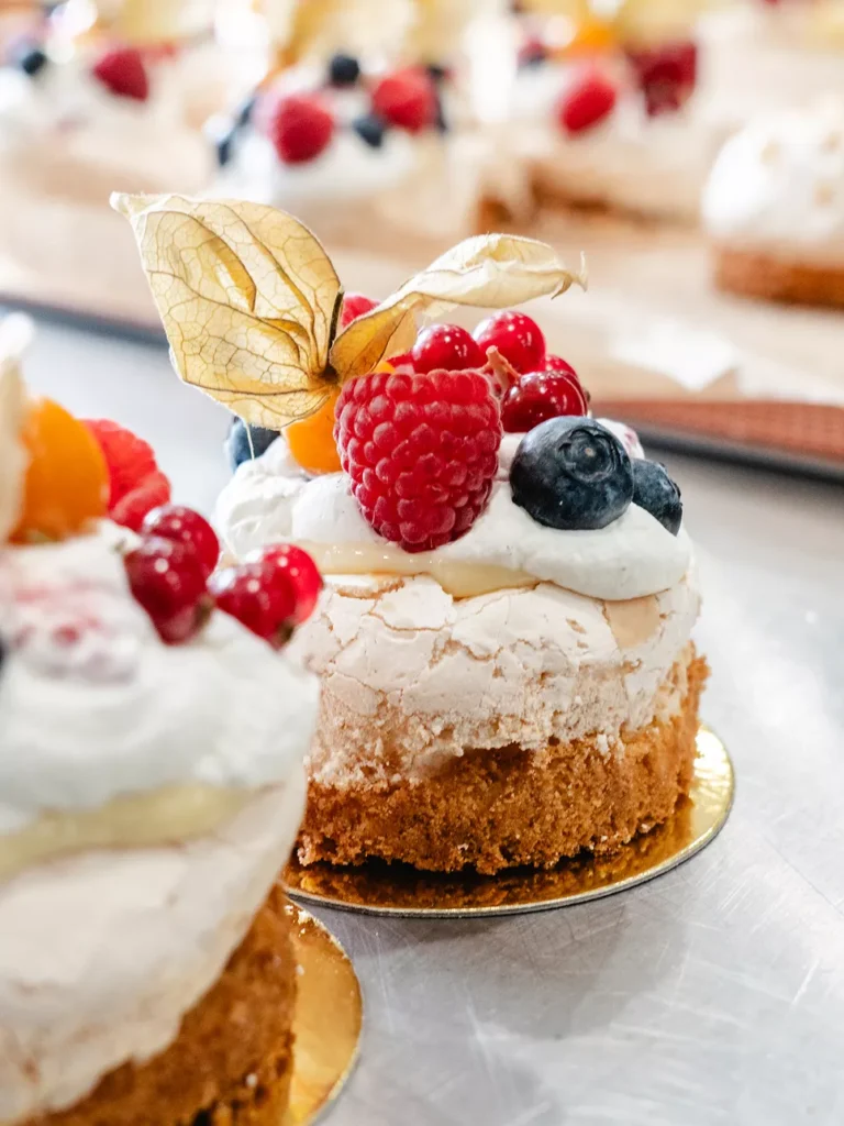Kleine Torte mit Baiser, Sahne und frischen Beeren, dekoriert mit Physalis auf goldenem Unterlage.