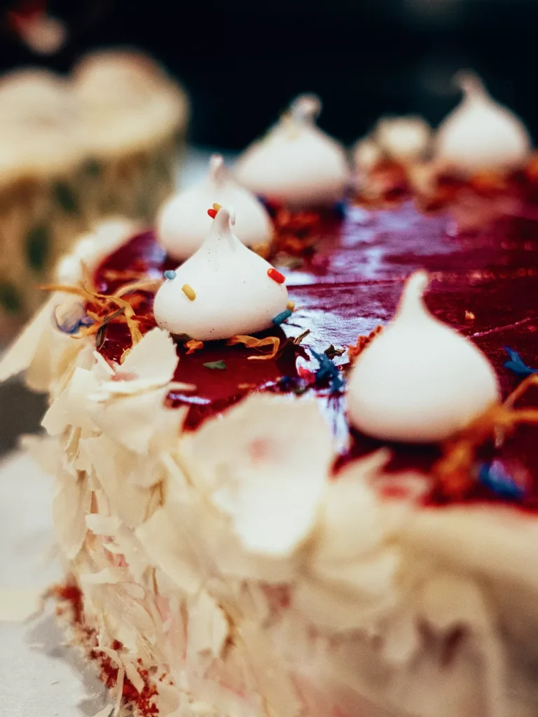 Eine Torte mit roter Glasur, dekoriert mit weißen Baisers und essbaren Blütenblättern.