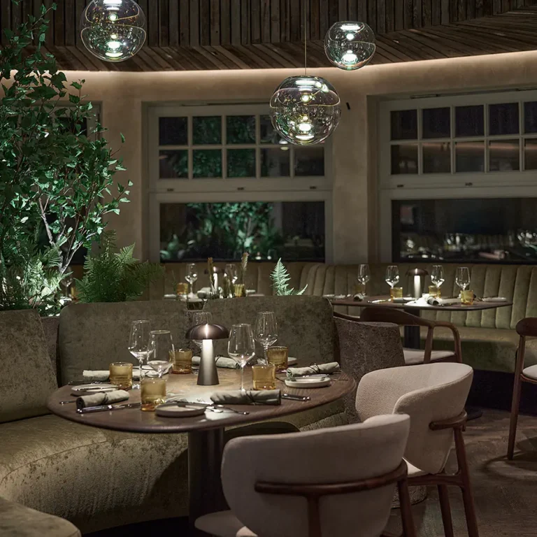 Elegantes Restaurant mit runden Tischen, sanfter Beleuchtung und gr&uuml;nen Pflanzen im Hintergrund.