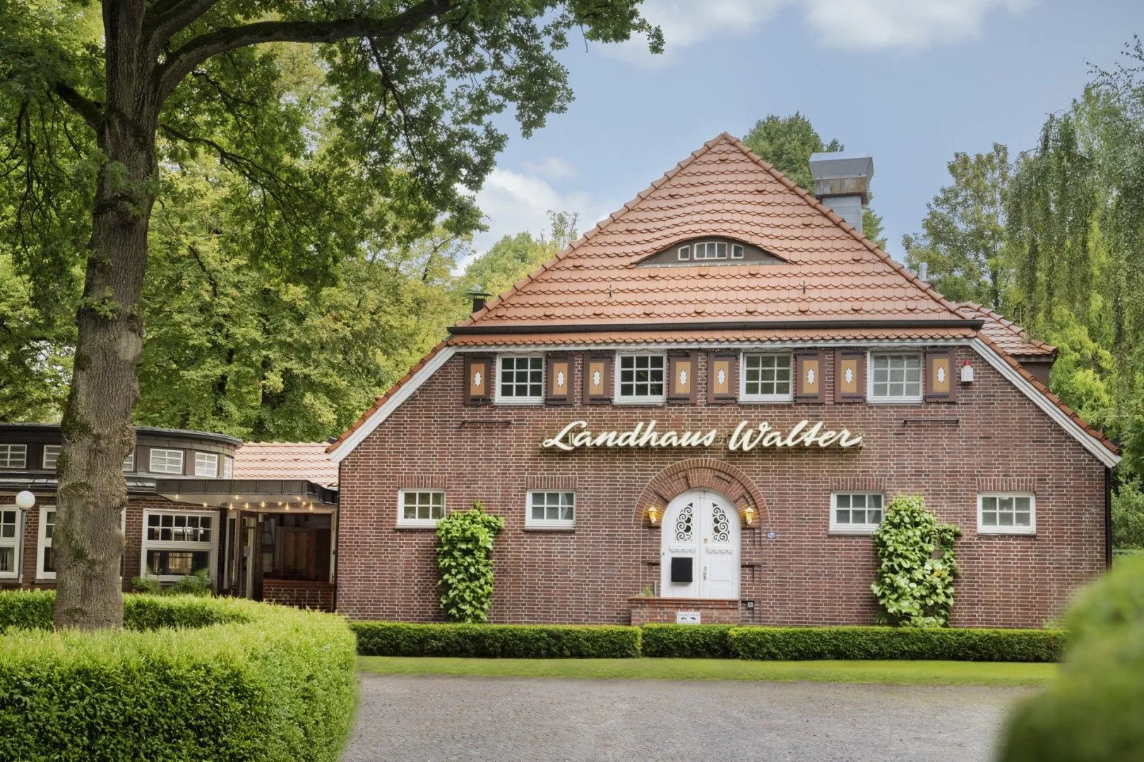 Ein rotes Backsteinhaus mit dem Schriftzug "Landhaus Walter", umgeben von Bäumen und einem gepflegten Garten.