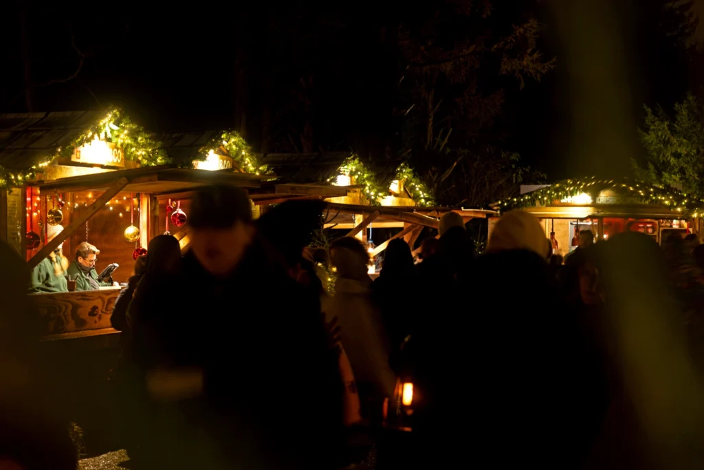 Weihnachtsmarkt bei Nacht mit festlich beleuchteten Ständen und Menschenmengen in winterlicher Atmosphäre.
