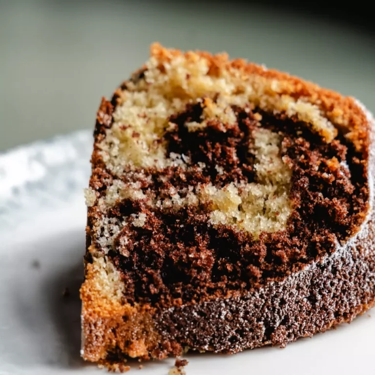 Ein St&uuml;ck Marmorkuchen auf einem wei&szlig;en Teller, mit einer gemusterten Mischung aus hellen und dunklen Teigschichten.