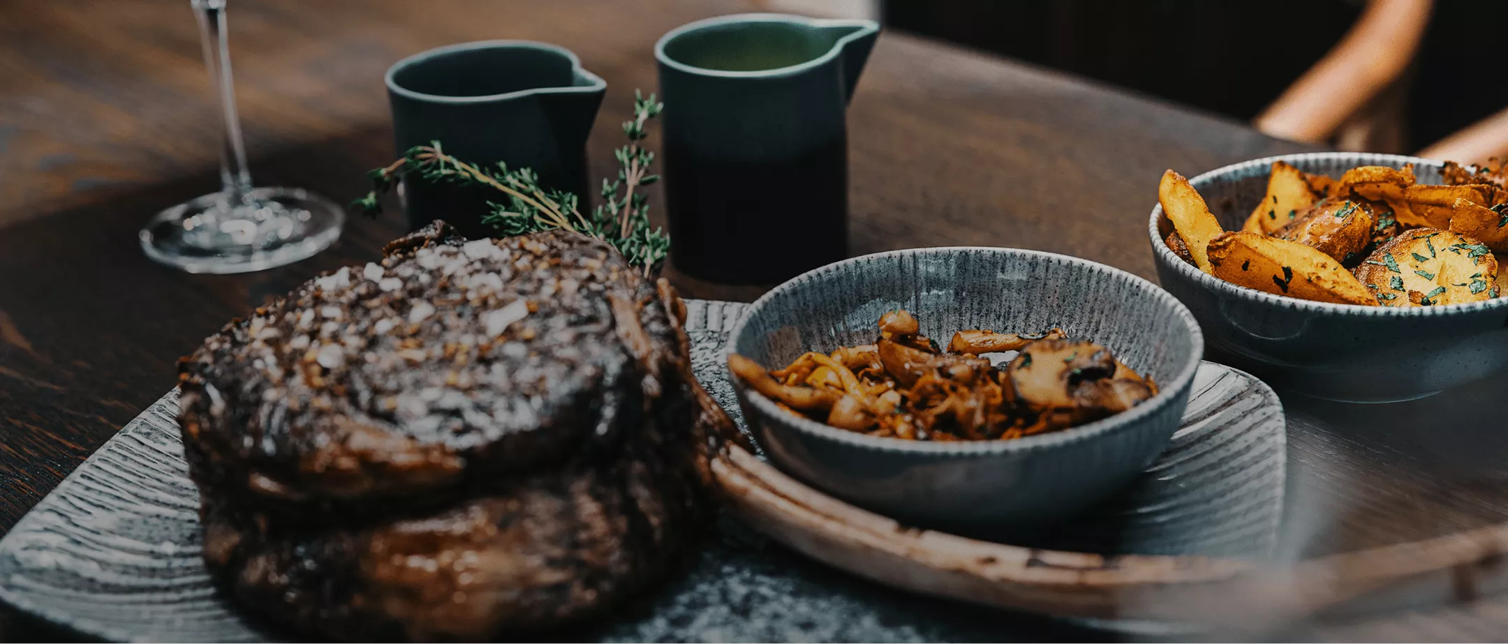 Zwei saftige Steaks auf einem Teller, begleitet von Pilzen und ger&ouml;steten Kartoffeln in Schalen.
