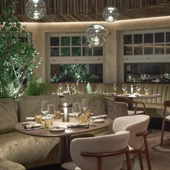 Elegantes Restaurant mit runden Tischen, edlen Gl&auml;sern und sanfter Beleuchtung, umgeben von Pflanzen.