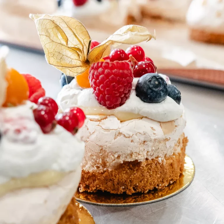 Kleine Torte mit einer Meringue-Oberfl&auml;che, dekoriert mit Beeren und einer physalis, auf goldenem Teller.